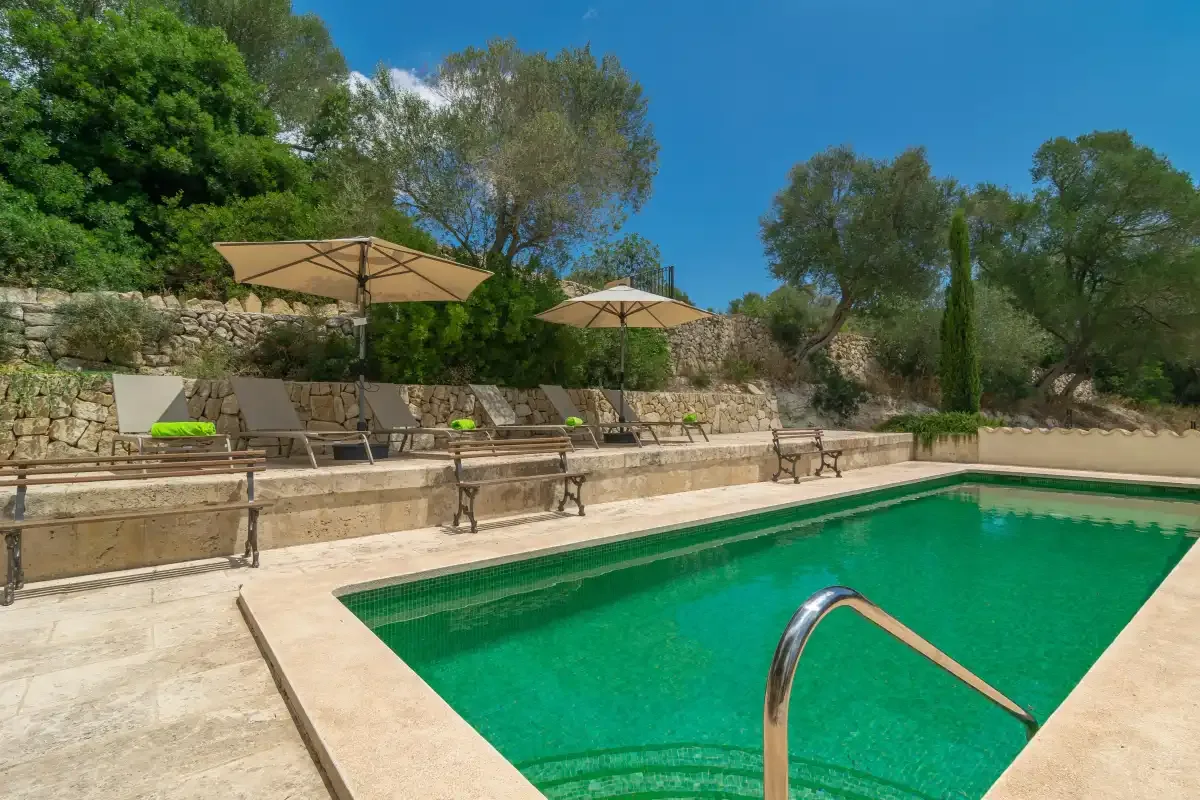 An outdoor swimming pool with lounge seating and umbrellas beside a stone wall.