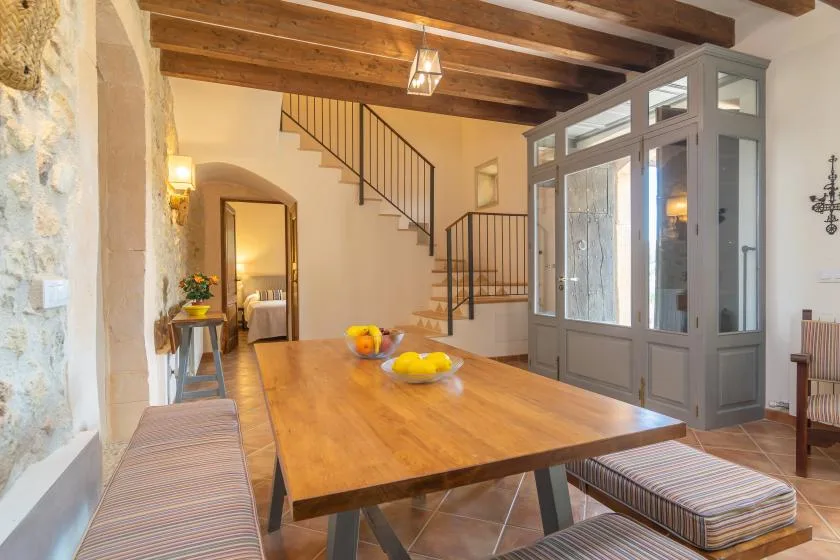 A dining area features a long wooden table beneath exposed ceiling beams.