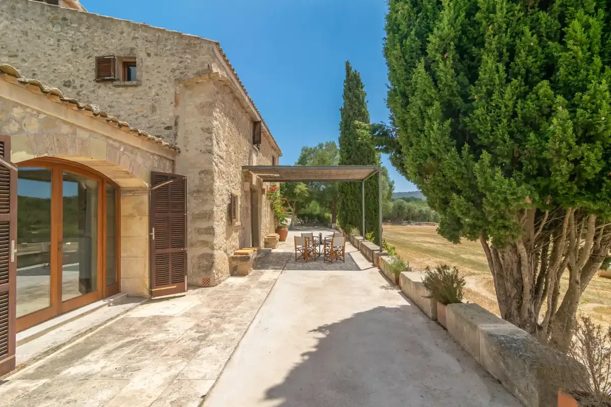 A stone house opens onto a sunny paved courtyard with outdoor seating.