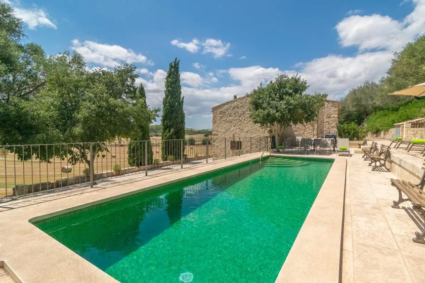 A swimming pool beside a stone building, with trees and outdoor seating.