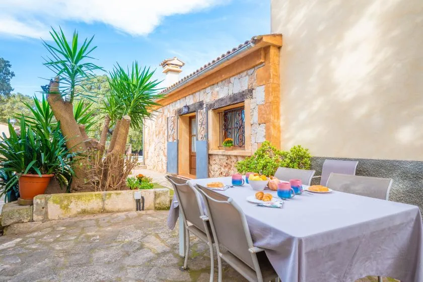 Comedor al aire libre con una mesa puesta junto a un edificio de piedra y plantas en macetas.