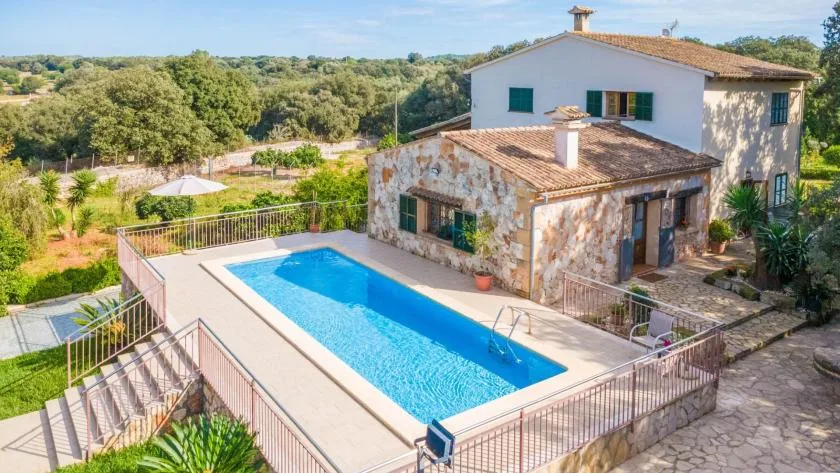 Una casa de piedra da a una piscina rectangular rodeada de vegetación.