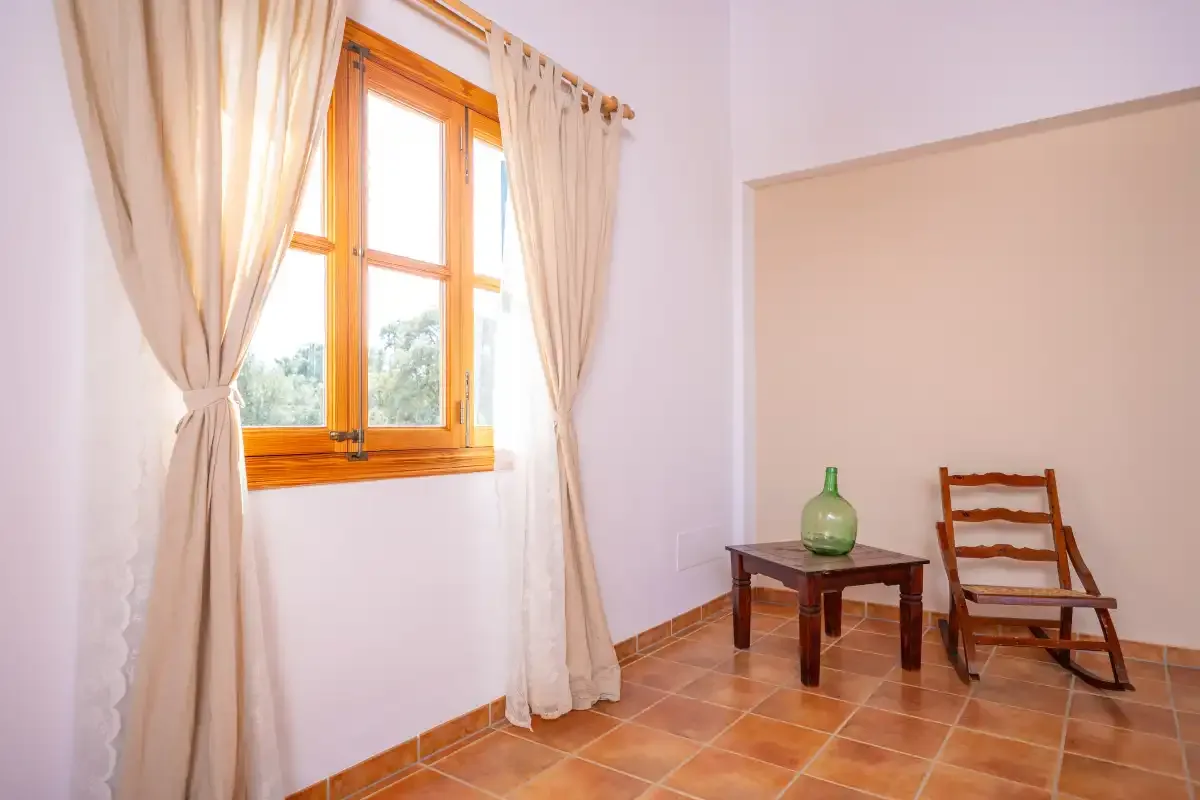 Una habitación luminosa con una ventana con cortinas, una mesa pequeña y una silla de madera.