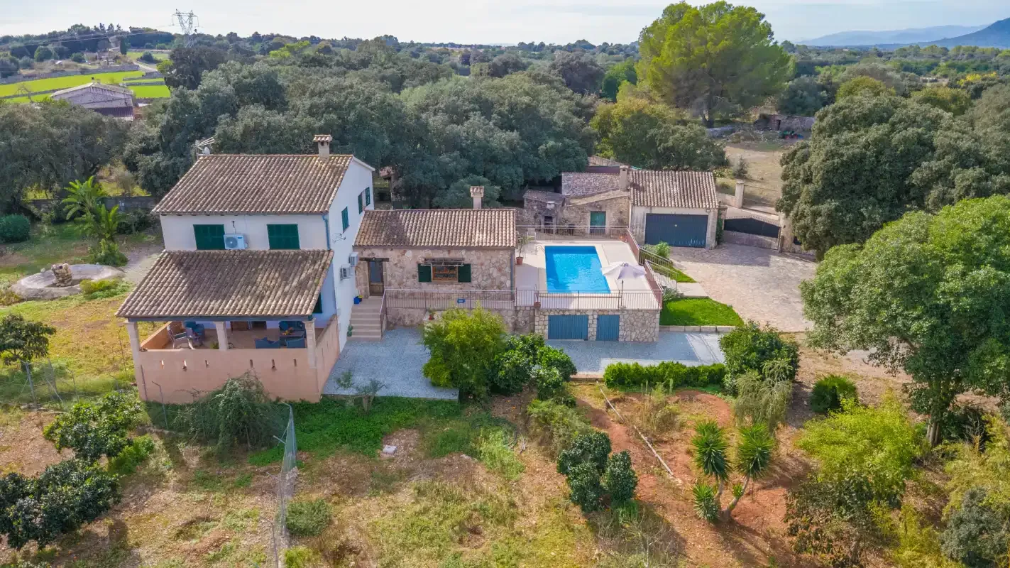 Una propiedad rural con varios edificios y una piscina está rodeada de árboles.