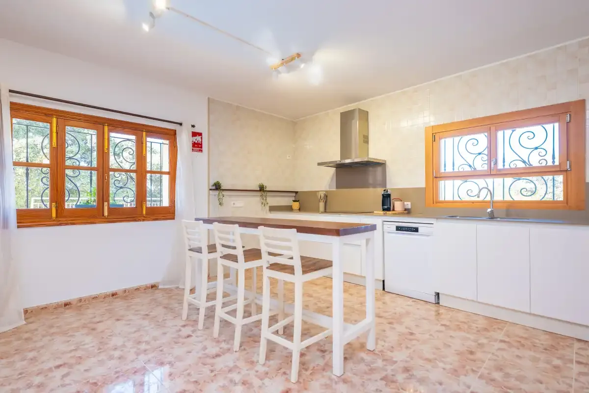 Una cocina luminosa con una isla central y asientos blancos.