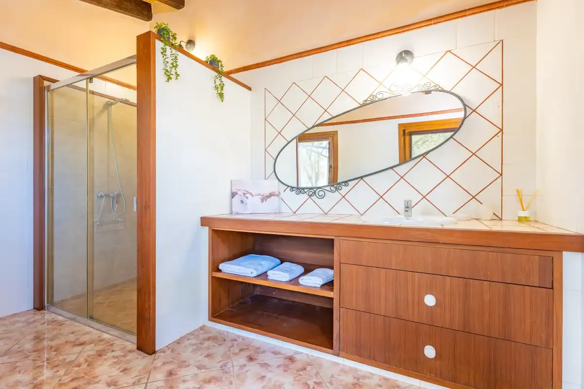 Un baño con ducha de vidrio, mueble de lavabo de madera y espejo.