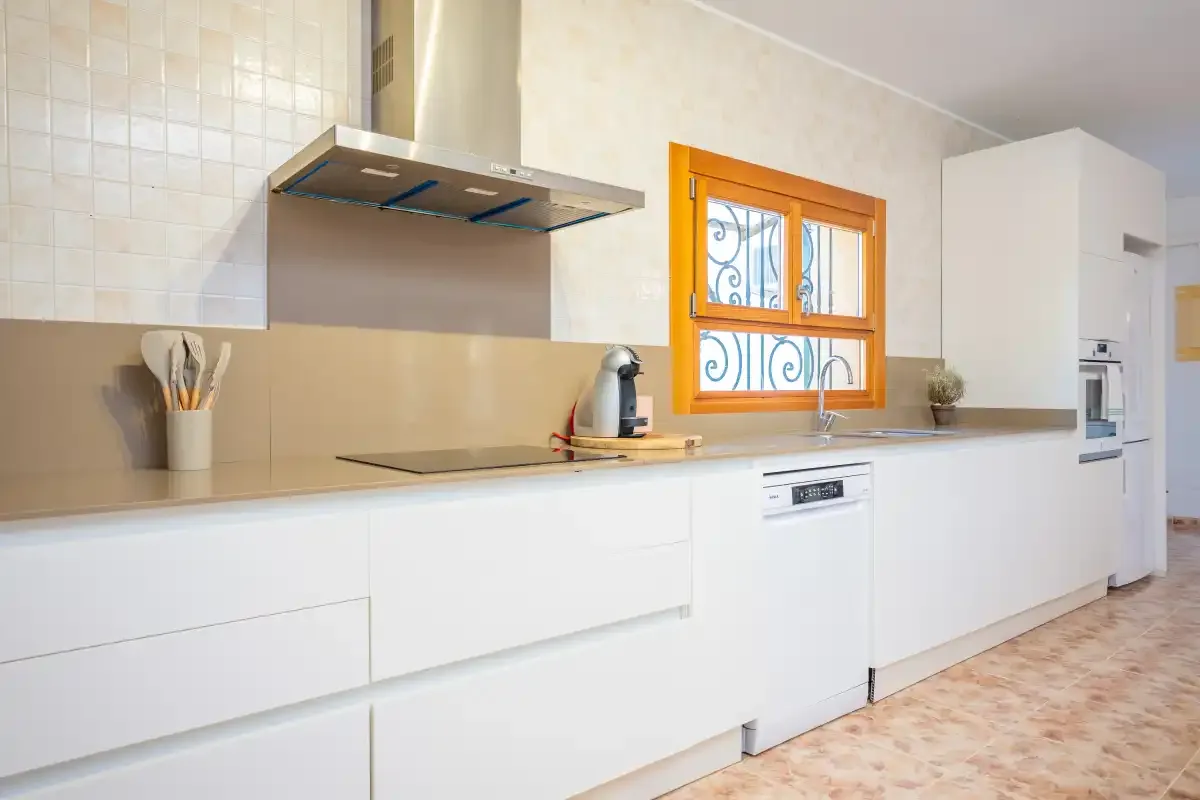 Una cocina luminosa con armarios blancos y una encimera bajo una ventana.