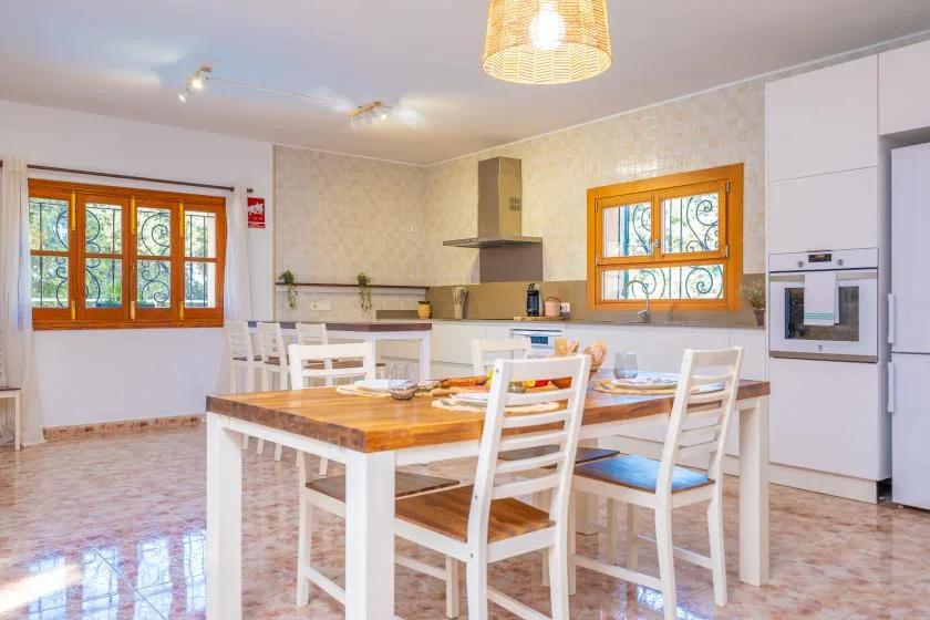 Una cocina luminosa con comedor, mesa de madera y asientos blancos.