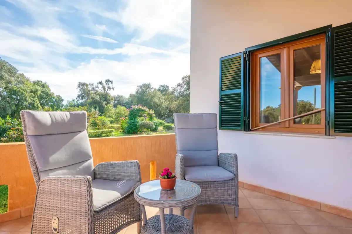 Una zona de estar en la terraza da a un jardín, junto a una ventana con contraventanas abiertas.