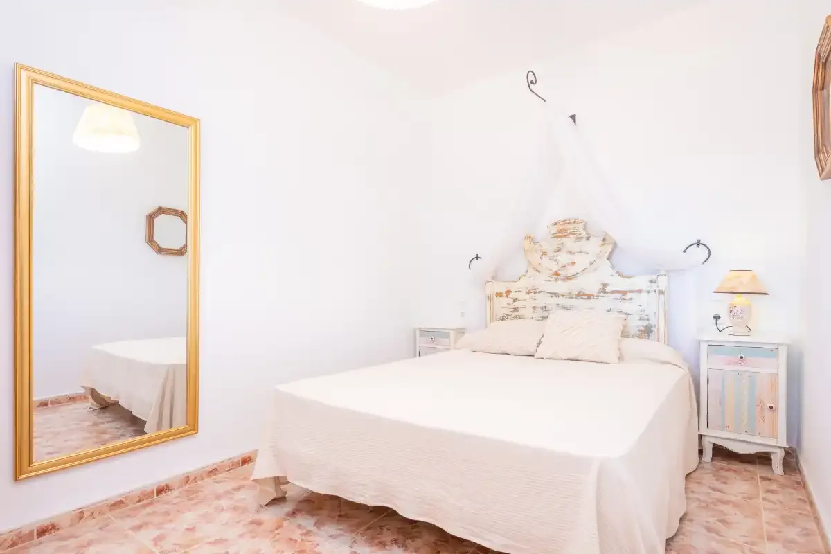 Un dormitorio luminoso con una cama y un espejo grande enmarcado.