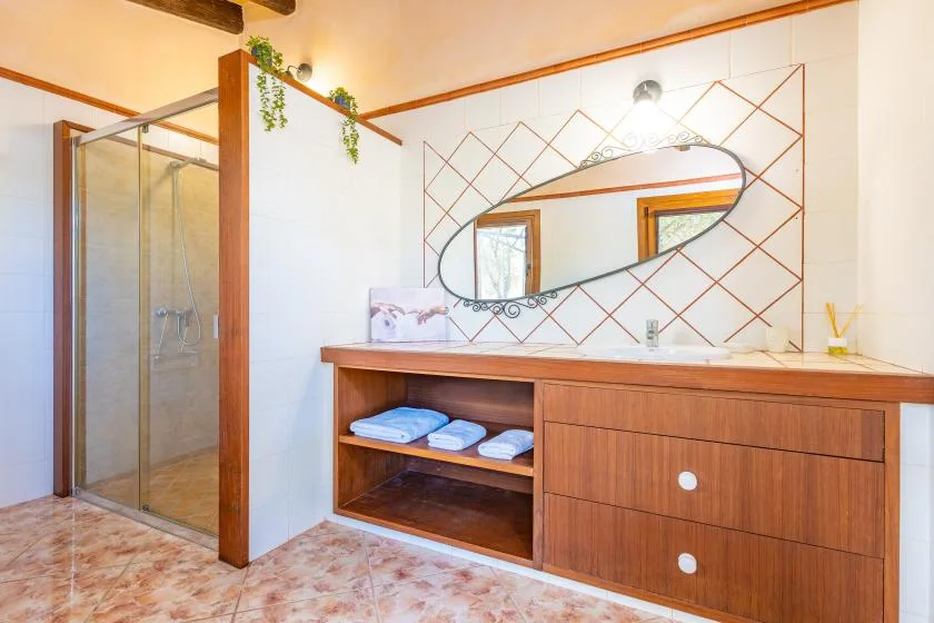 Un baño luminoso con una ducha de vidrio y un mueble de madera bajo un espejo grande.