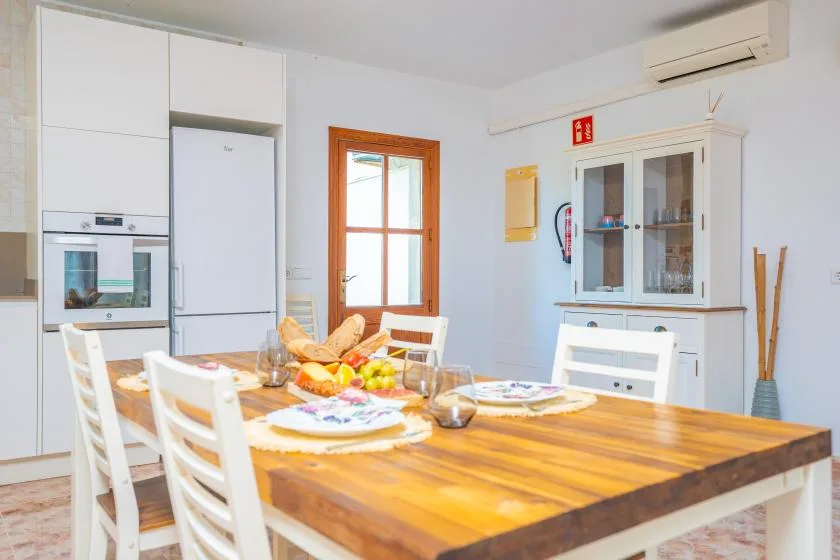 Un comedor luminoso con una mesa de madera junto a armarios blancos de cocina.