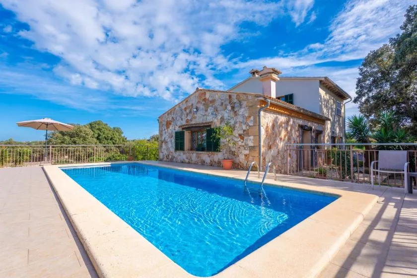 Una piscina junto a una casa con fachada de piedra y asientos en el patio.