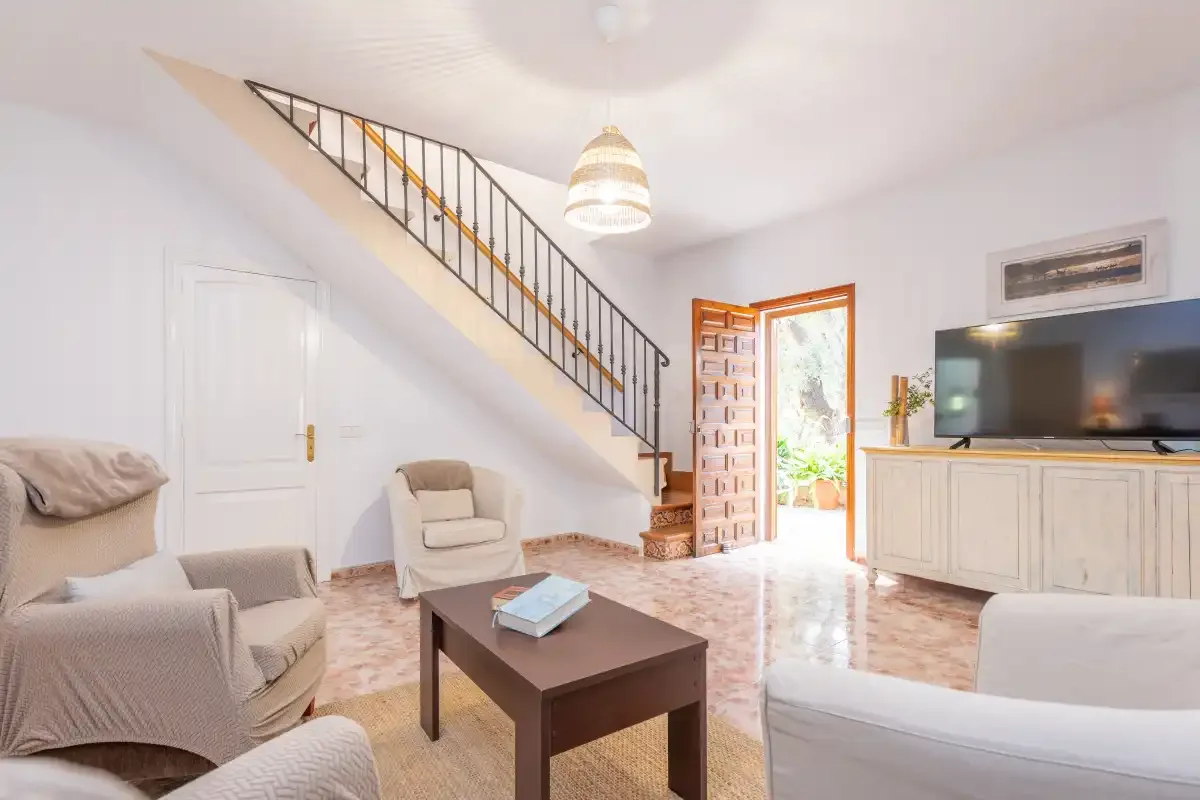 Sala de estar con asientos, una mesa de centro y una escalera junto a una puerta abierta.