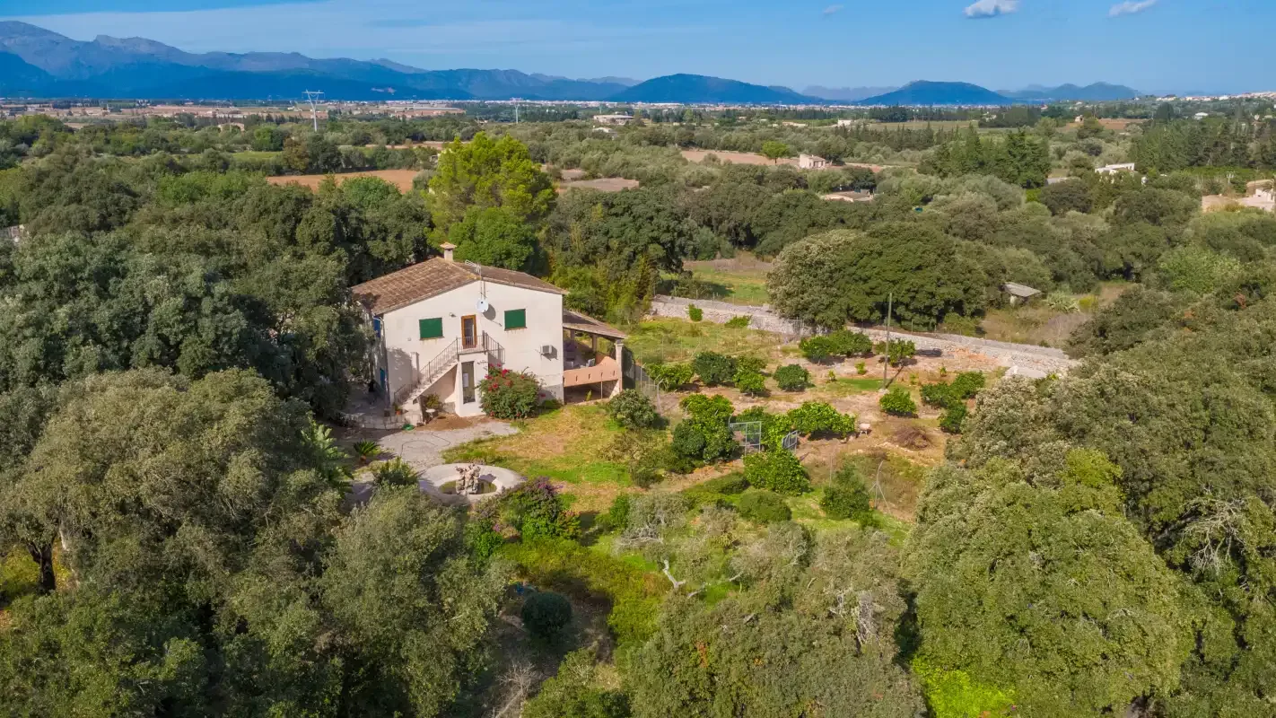 Vista aérea de una casa rural rodeada de árboles y campos.