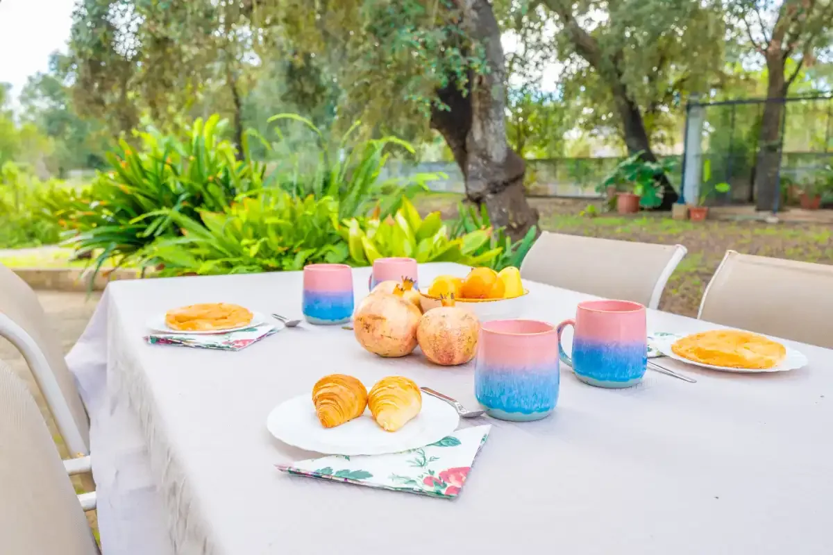 Una mesa al aire libre está preparada con platos, fruta y vasos de colores.