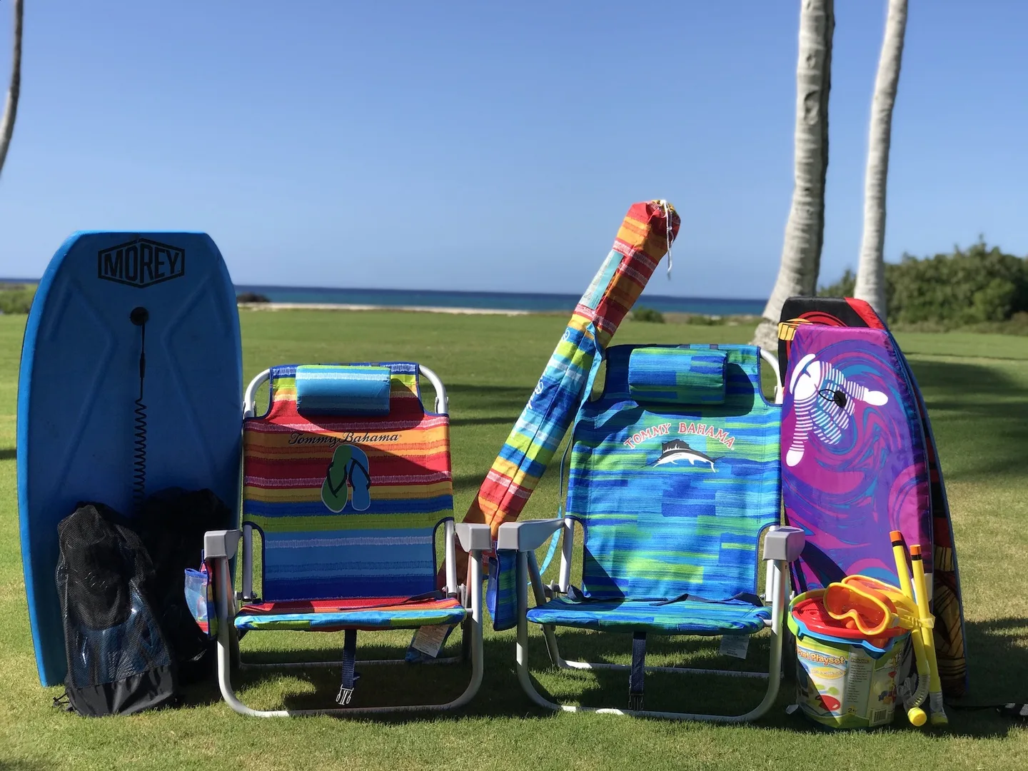 Sillas de playa y tablas coloridas están sobre el césped junto al mar.