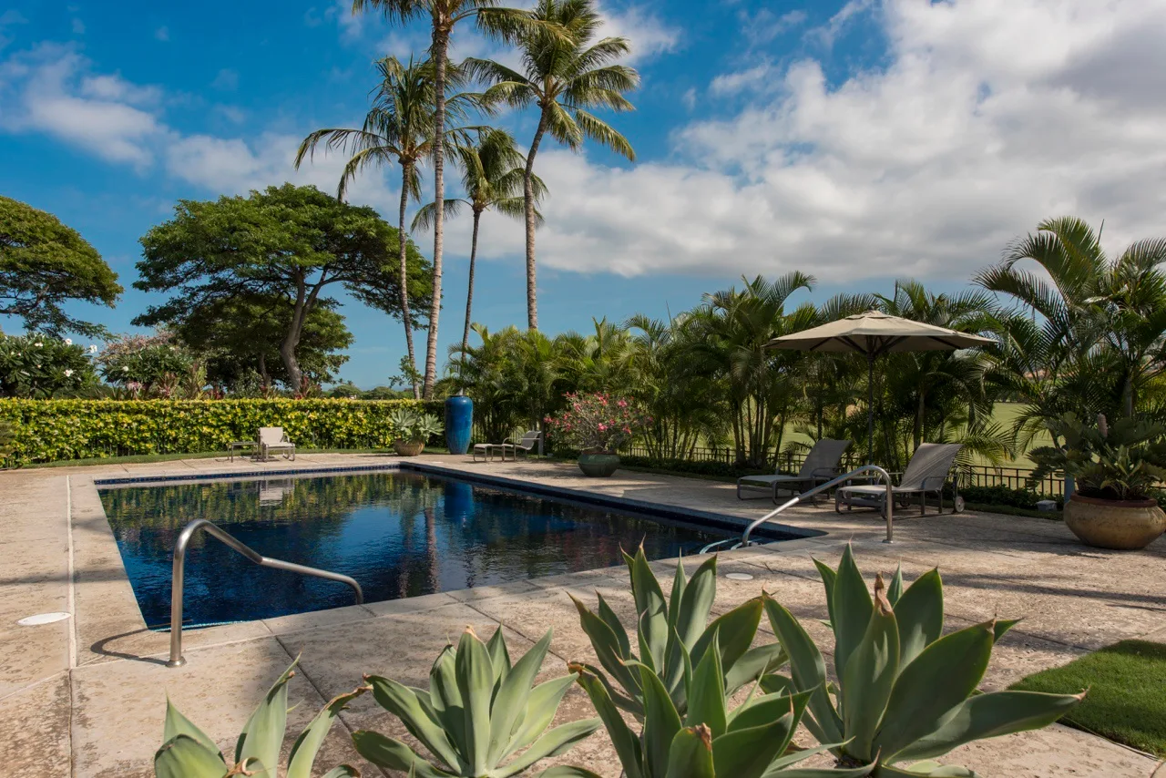 Una piscina está rodeada de plantas tropicales bajo un cielo parcialmente nublado.