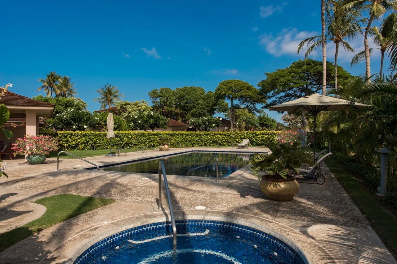 Una zona de piscina al aire libre con una piscina curva, tumbonas y vegetación tropical.