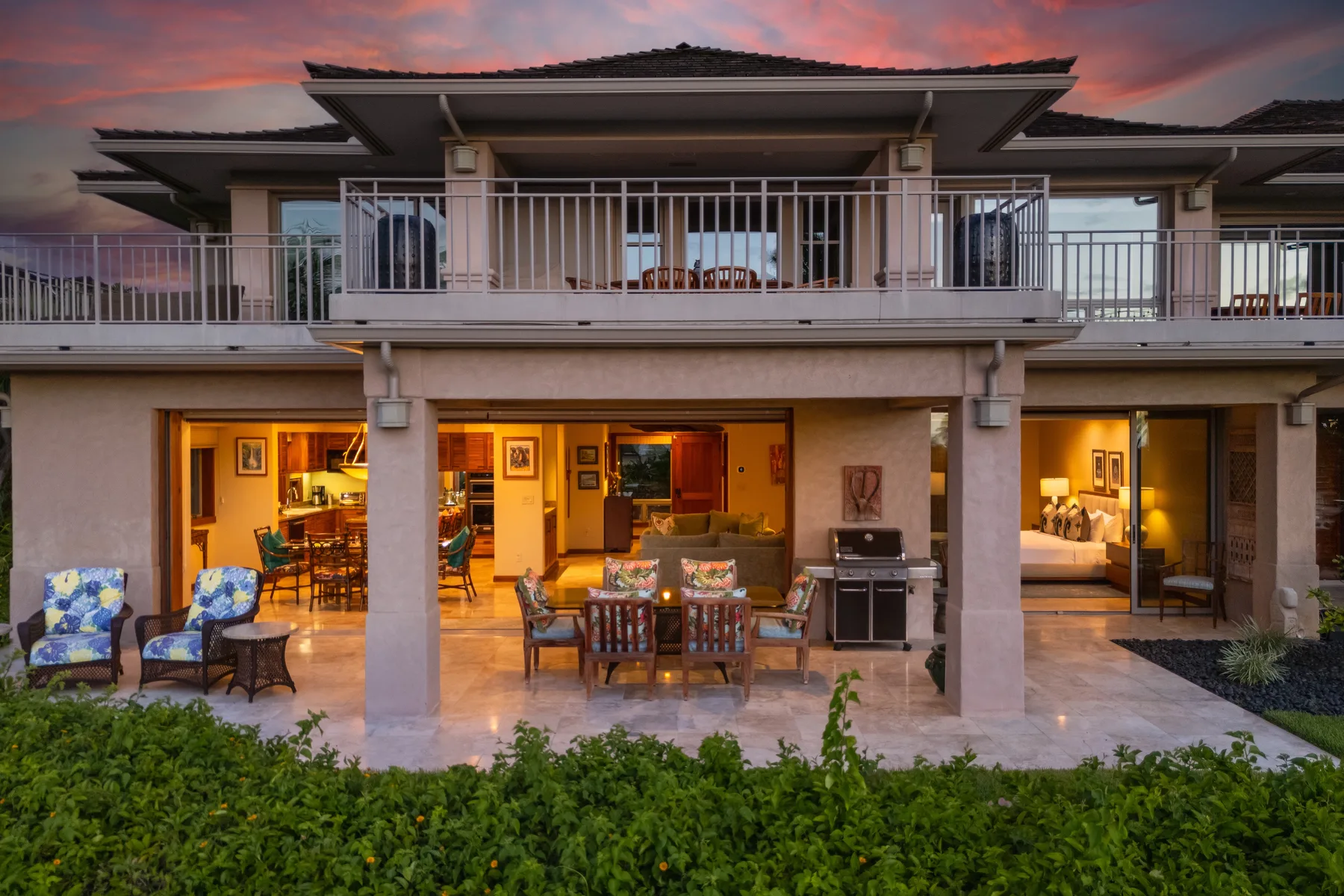 Casa de dos niveles con asientos en un patio abierto y un balcón al atardecer.