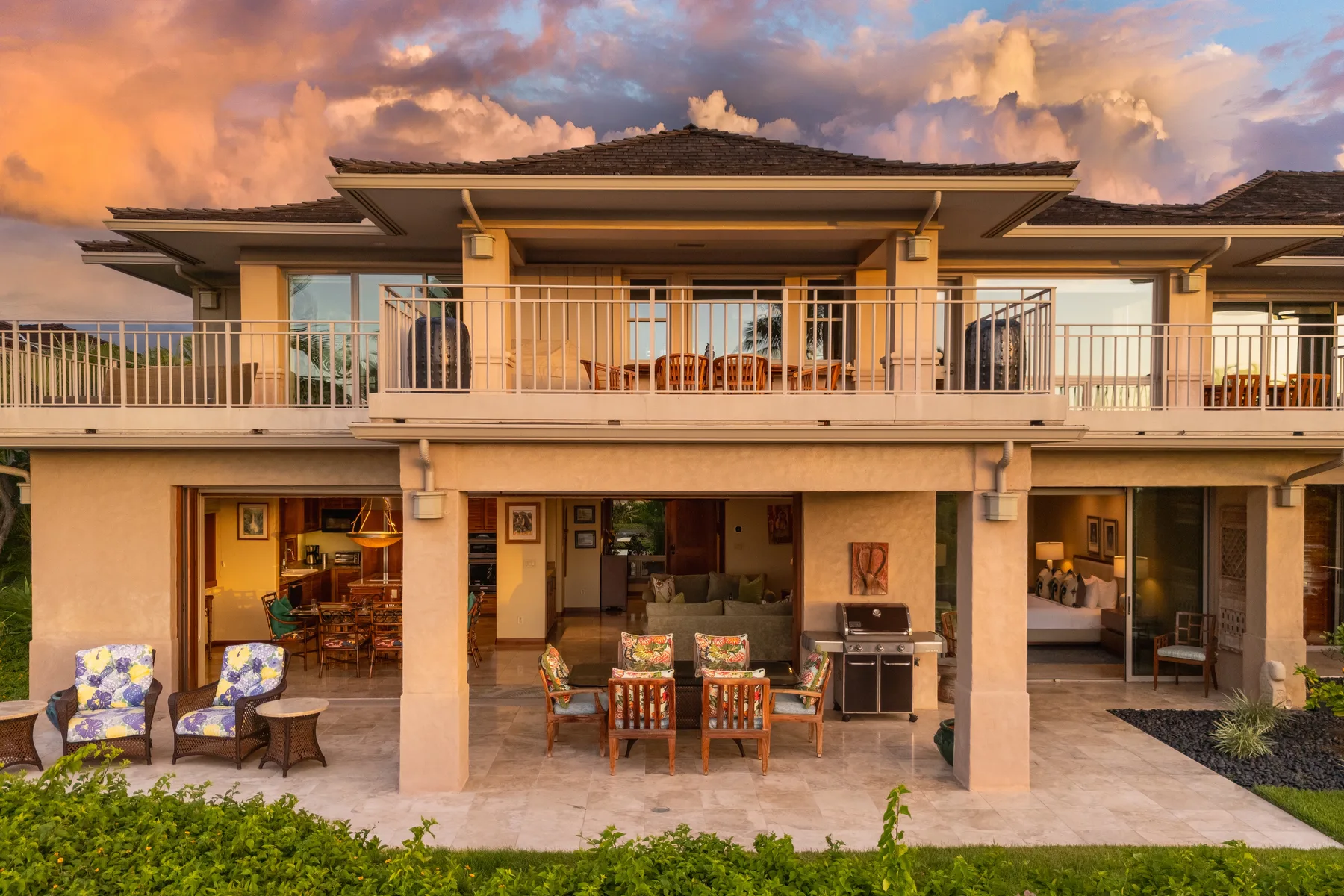 Una casa de dos pisos con asientos en un patio abierto bajo un cielo colorido al atardecer.