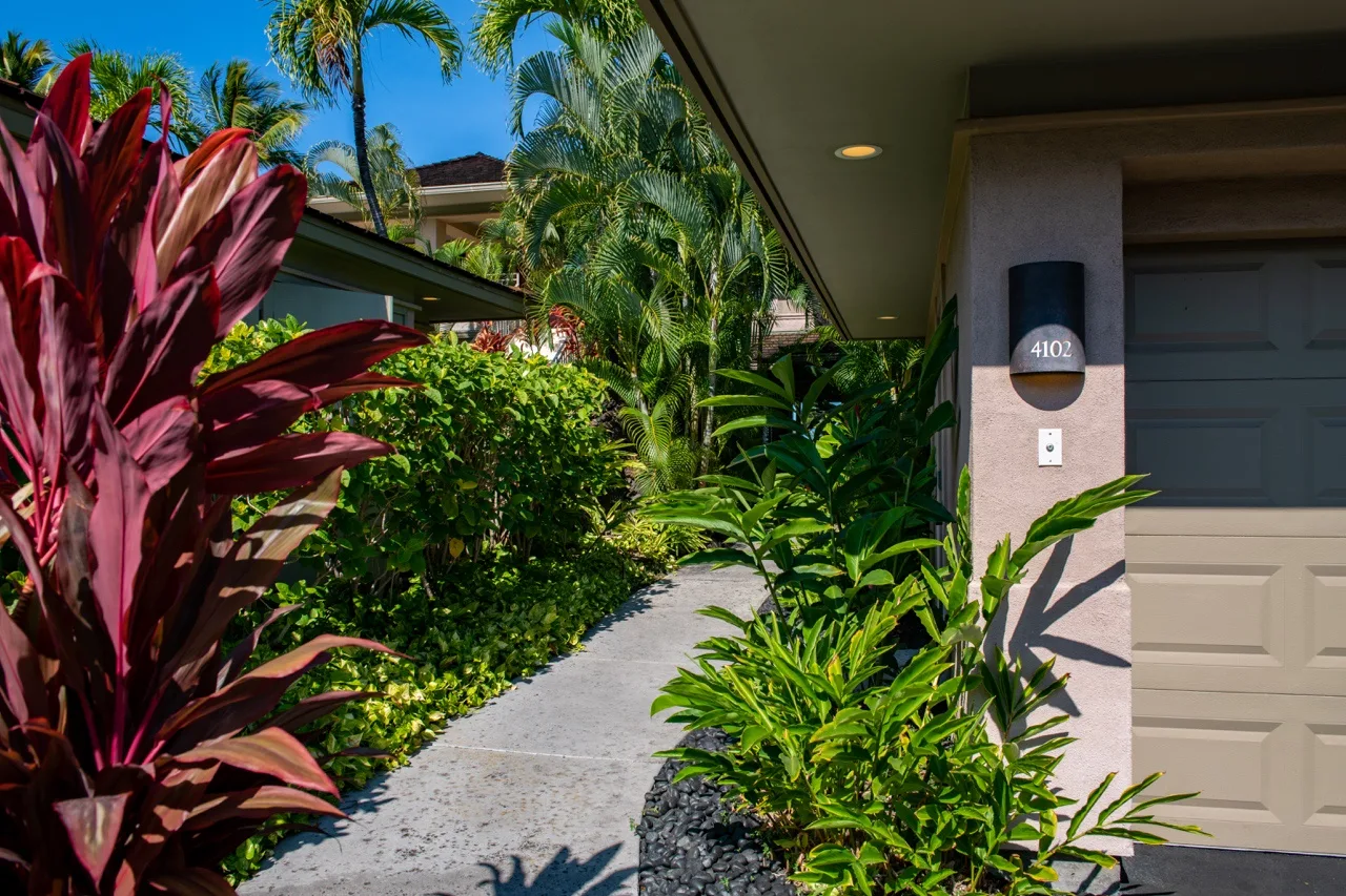 Un sendero de jardín pasa junto a plantas tropicales y conduce a la entrada de una casa.