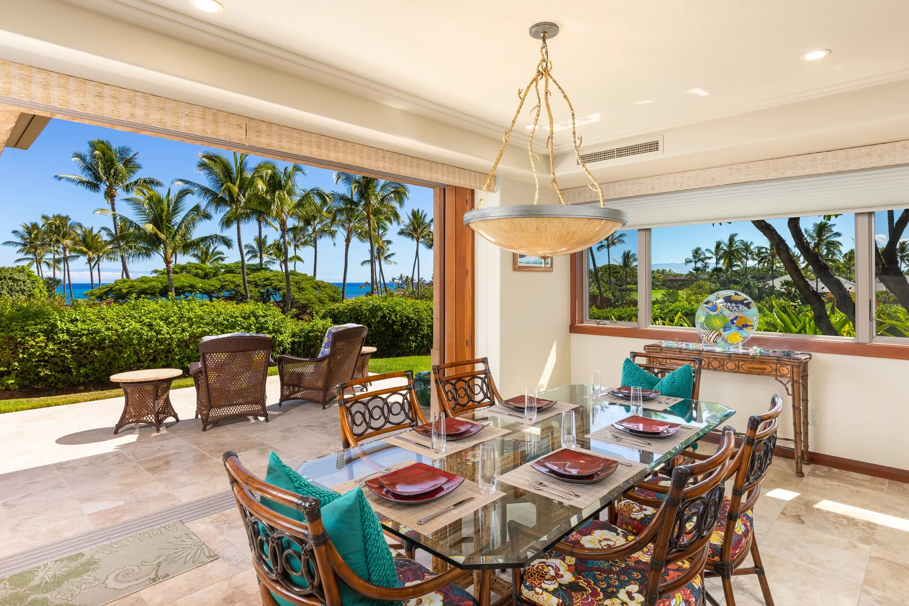 Comedor con mesa de vidrio y grandes ventanas con vista a la vegetación tropical.