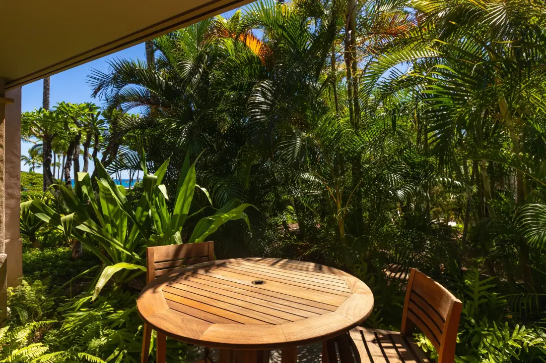 Un patio al aire libre con una mesa redonda de madera y abundantes plantas tropicales.