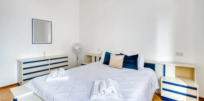A bedroom with a neatly made bed, folded towels, and a dresser.