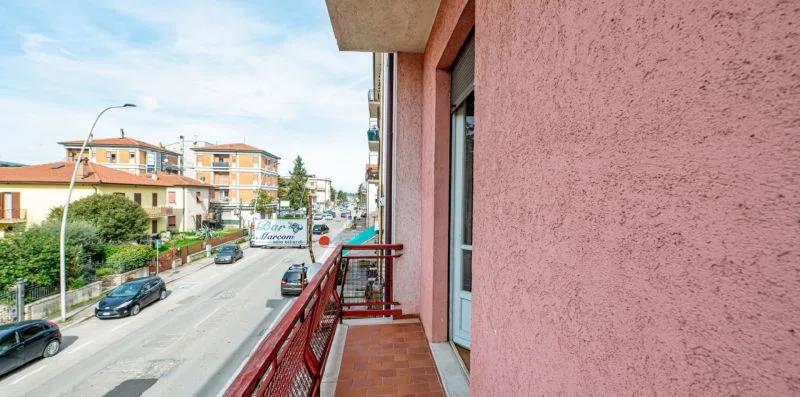 A small balcony overlooks a street lined with buildings and trees.