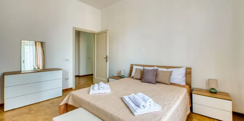 A bedroom with a double bed, folded towels, and a white dresser.