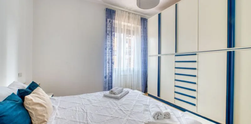 A bedroom with a neatly made bed and a window with blue curtains.