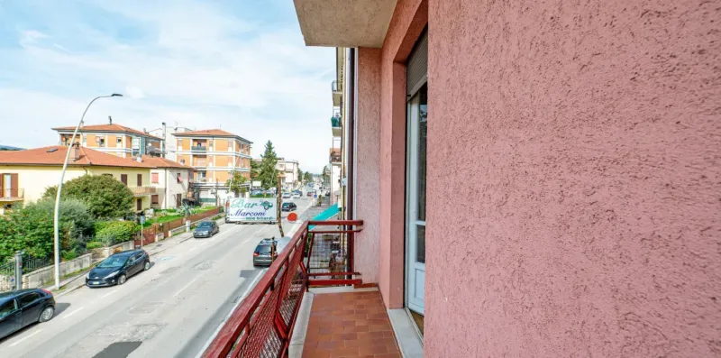 A narrow balcony overlooks a residential street, with a red railing along the edge.