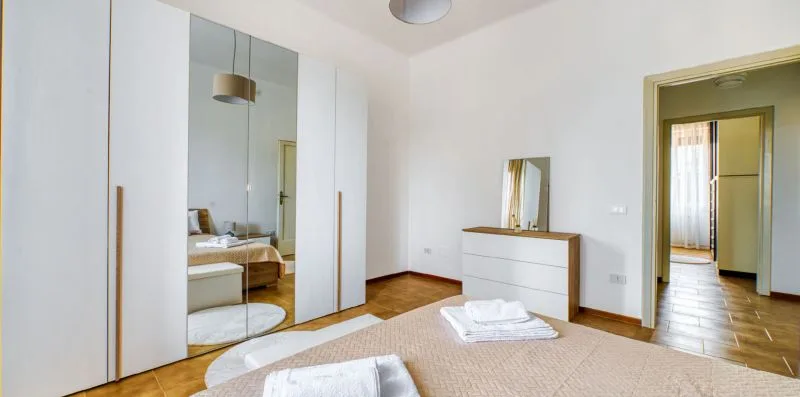 A bright bedroom with a bed, mirrored wardrobe, and doorway to a hall.