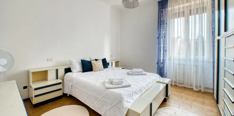 A bedroom with a large bed dressed in white and tall curtained windows.