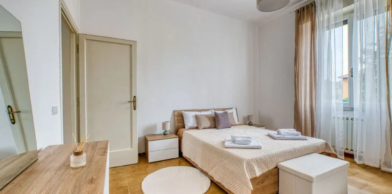 A bedroom with a bed, bedside tables, and a large window with curtains.