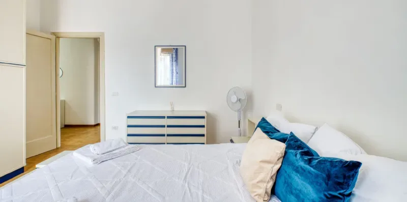A bright bedroom with a neatly made bed and blue accent pillows.