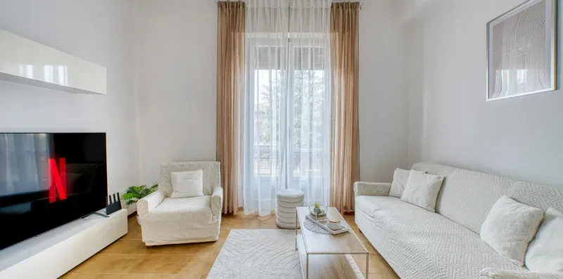 A living room with seating around a coffee table and a tall curtained window.