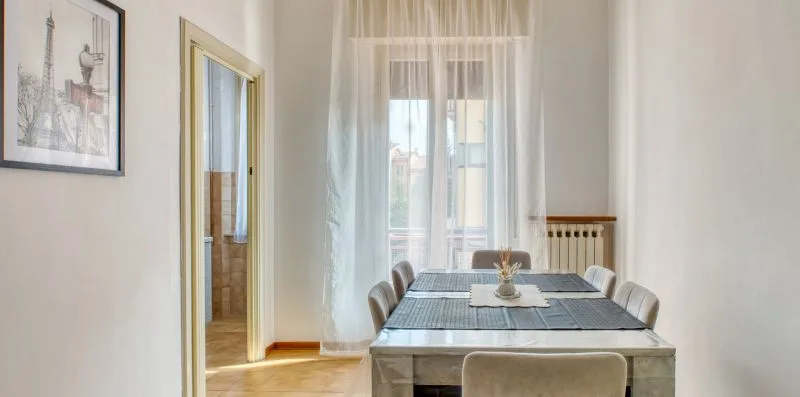 A dining area with a table set beneath a sheer-curtained window.