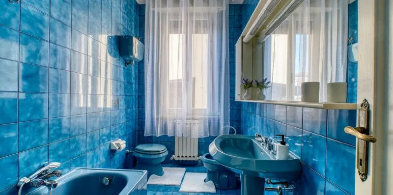 A blue-tiled bathroom with a bathtub, sink, and window.