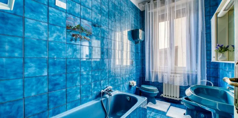 A blue-tiled bathroom with a bathtub, sink, and window.