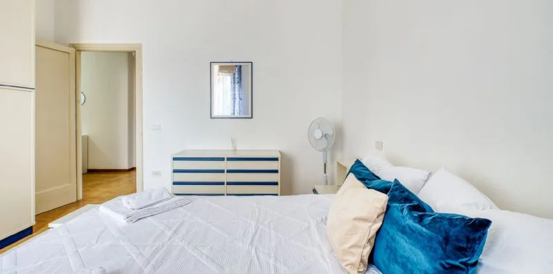 A bedroom with a neatly made bed and blue accent pillows.