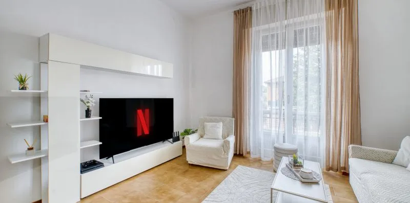 A bright living room with a television, seating, and tall curtained windows.