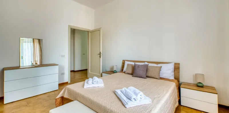 A bedroom with a neatly made bed and white bedside drawers.
