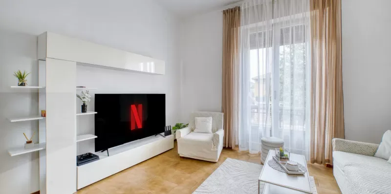 A bright living room with a television, seating, and tall curtained windows.