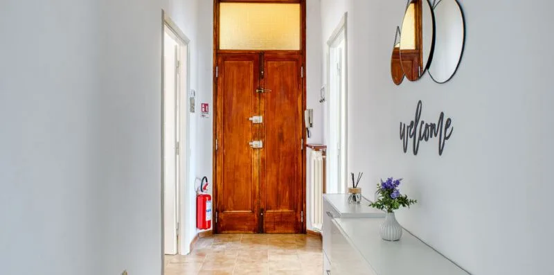 A bright hallway features a wooden entrance door and a console table with flowers.