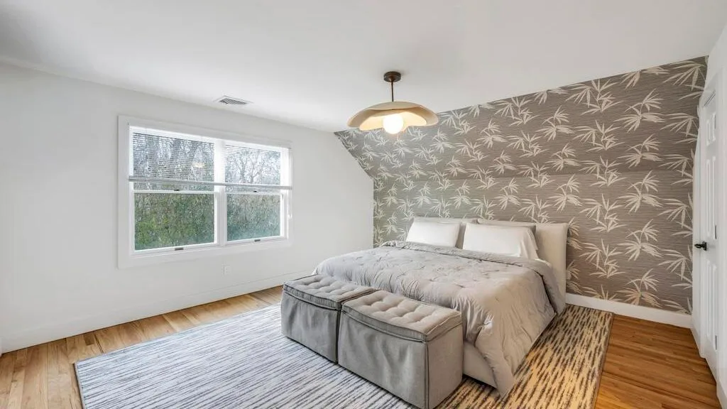 Un dormitorio con una cama, dos bancos tapizados y papel tapiz estampado.