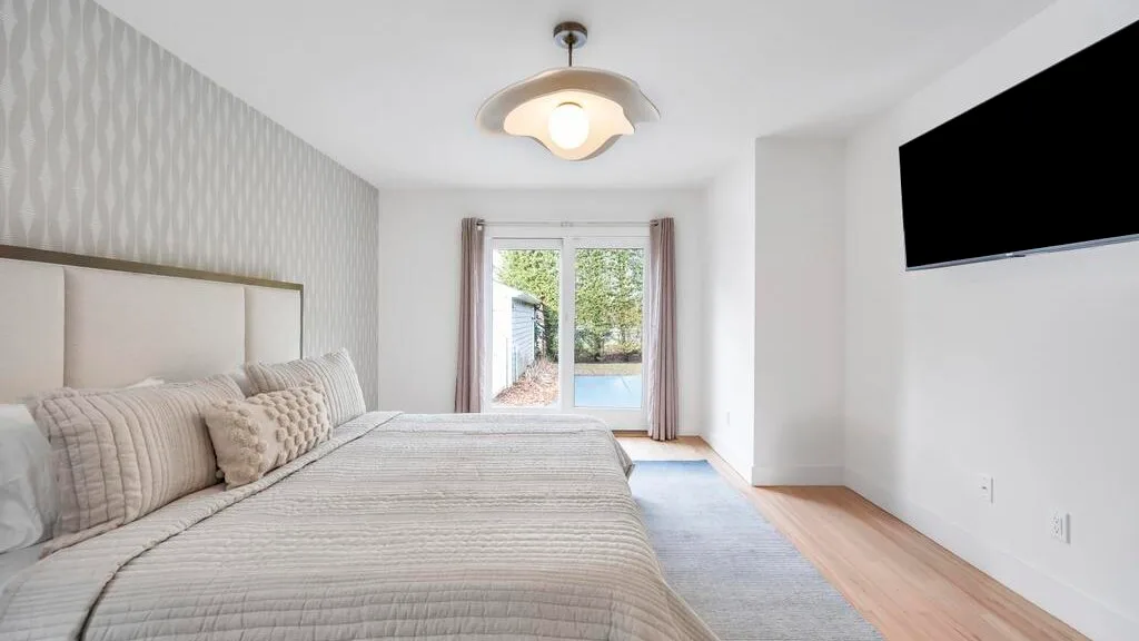 Un dormitorio con una cama grande, un televisor y una ventana con vista a la vegetación.