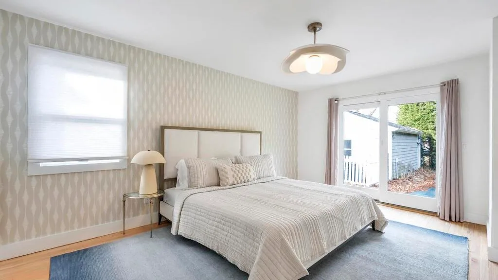 Un dormitorio luminoso con una cama bien tendida y ventanas grandes.