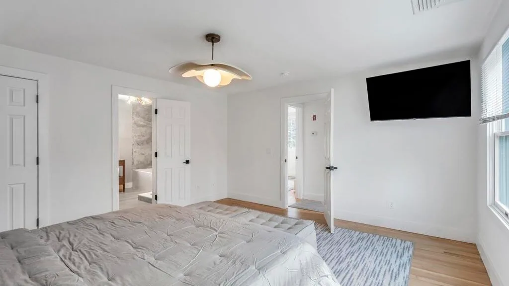 Un dormitorio luminoso con una cama grande y un televisor en la pared.